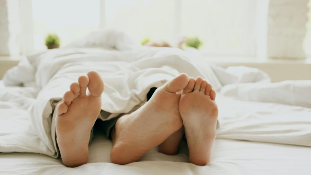 Relaxed couple's feet peeking from under a blanket, cozy indoor morning.
