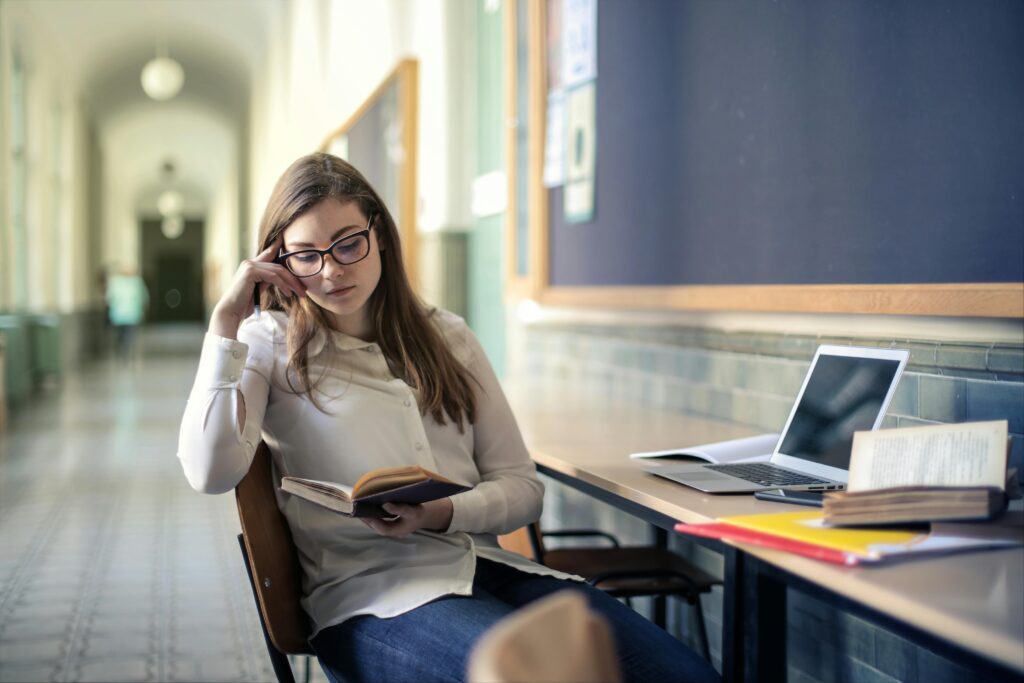 A young woman studies diligently in a university hallway, reading a book.