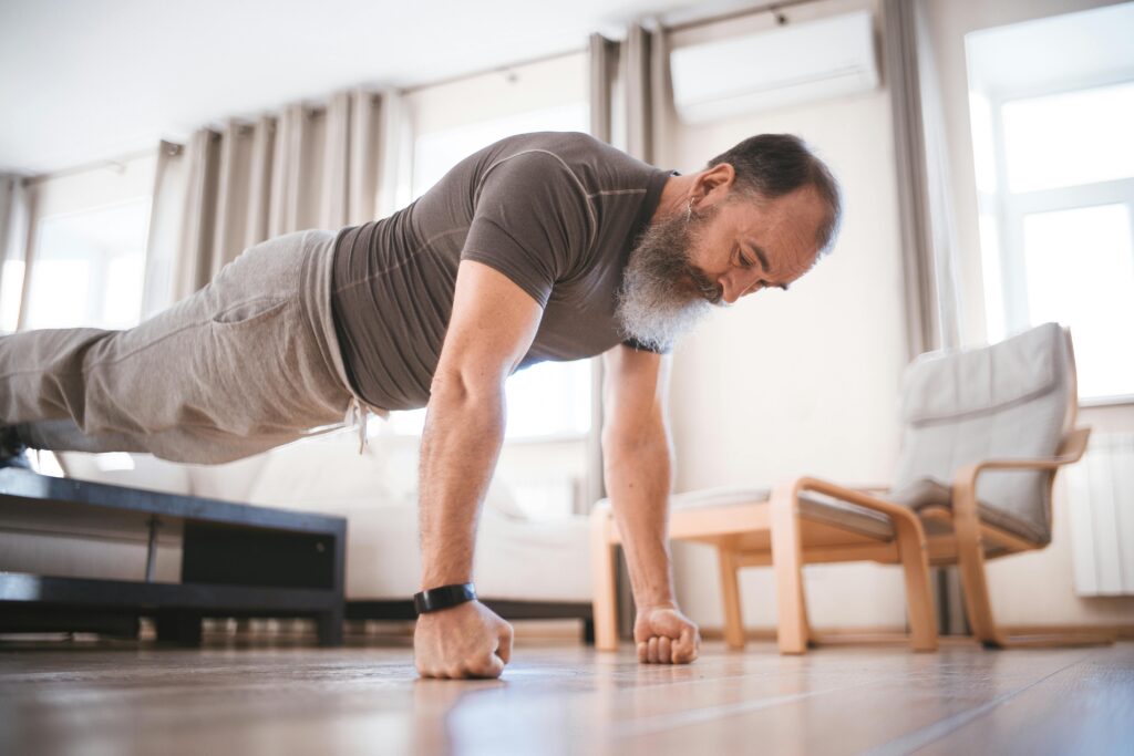 Elderly man performing push-ups at home in a bright and airy living room.